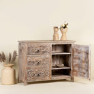 Open doors image of a hand-carved sideboard made from mango wood, featuring intricate geometric and floral patterns across the drawers and cabinet door, with a distressed whitewashed finish that enhances its vintage artisanal appeal.
