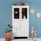 A vintage-style reclaimed teak wood showcase cabinet with glass doors and various decorative items displayed on its shelves, set against a plain blue wall.