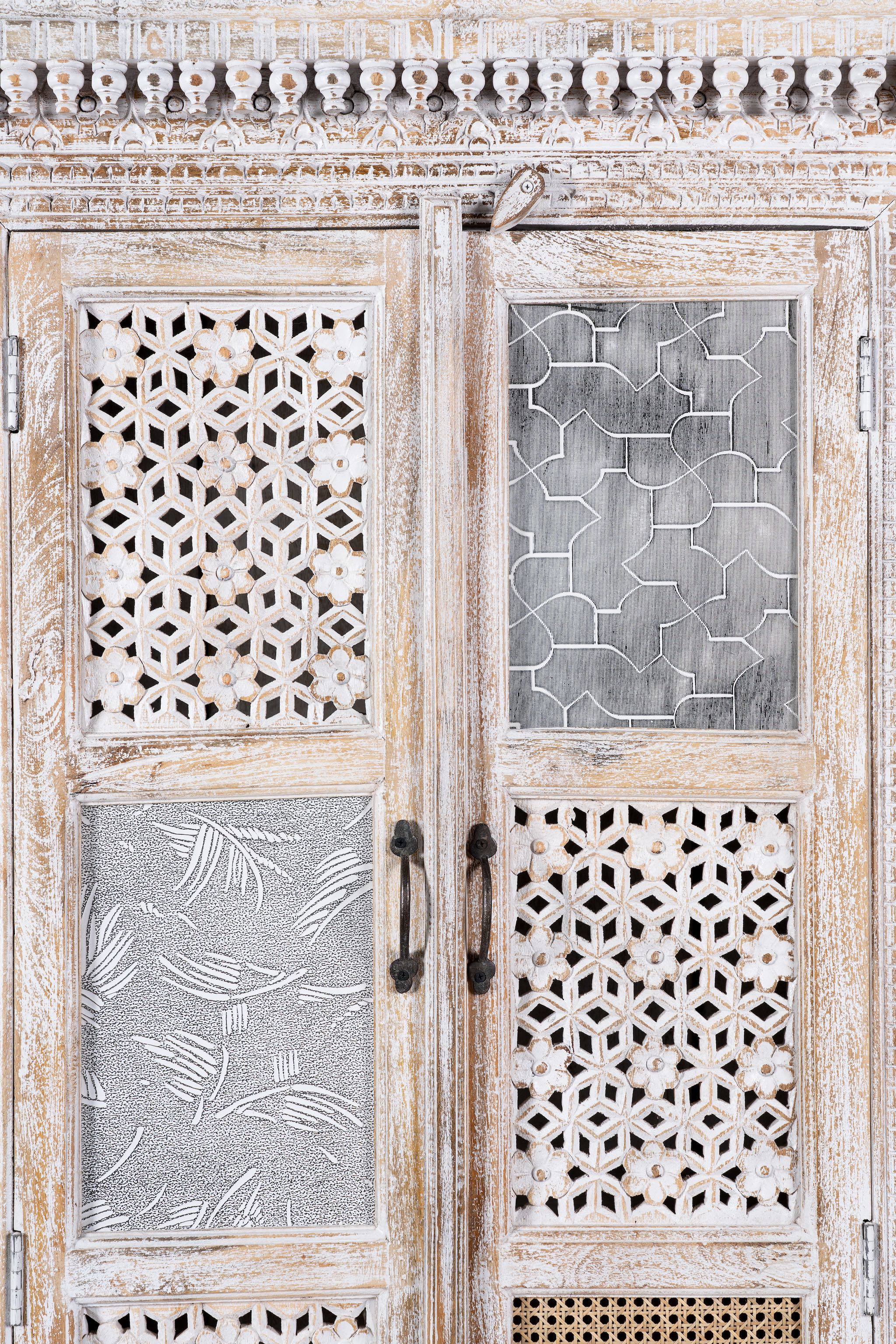 Close up image of a whitewashed mango wood cabinet with hand-carved details, rattan inserts, and glass panels; versatile as bedroom furniture or wooden wardrobe; 192 × 110 × 40 cm.