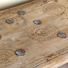 Close up image of a sandblasted teak wood coffee table crafted from a hand-carved antique Indian door, featuring intricate traditional motifs and a rustic finish. A reclaimed wood furniture piece that blends cultural heritage with sustainable design.