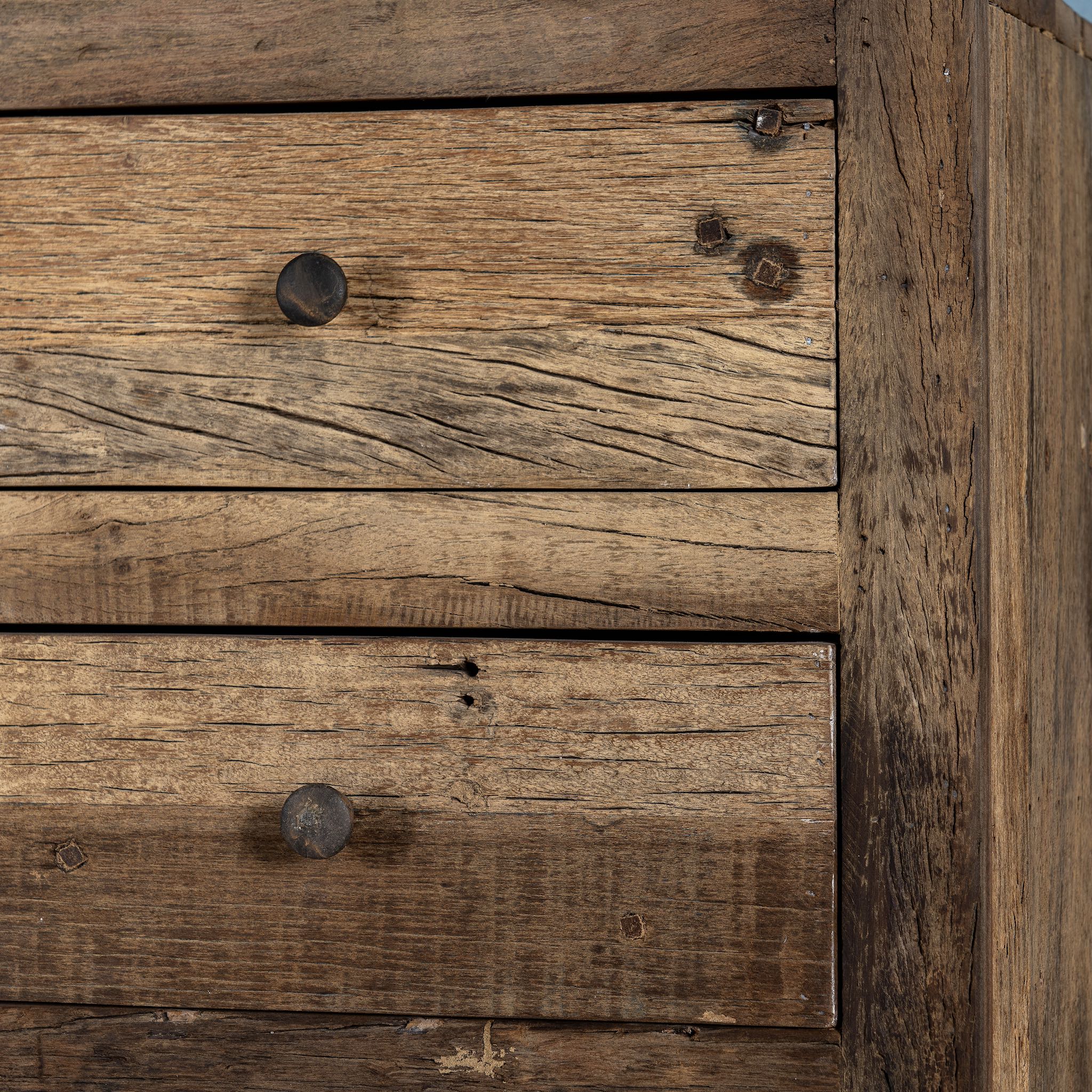 Close up image of a Wabi-Sabi style chest of drawers crafted from recycled old wood, featuring six drawers with a natural, weathered driftwood finish and visible wood grain variations.


