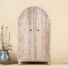 Arched wardrobe made from solid mango wood, featuring intricate hand-carved floral and leaf motifs on double doors, finished in a soft natural tone- ideal for Ibiza or boho interiors.
