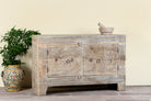 Side angle image of a handcrafted sideboard Tanay made from reclaimed teak wood, featuring antique Indian door fronts with original carvings. A Mediterranean-inspired piece of unique Indian furniture with sustainable character and functional storage.