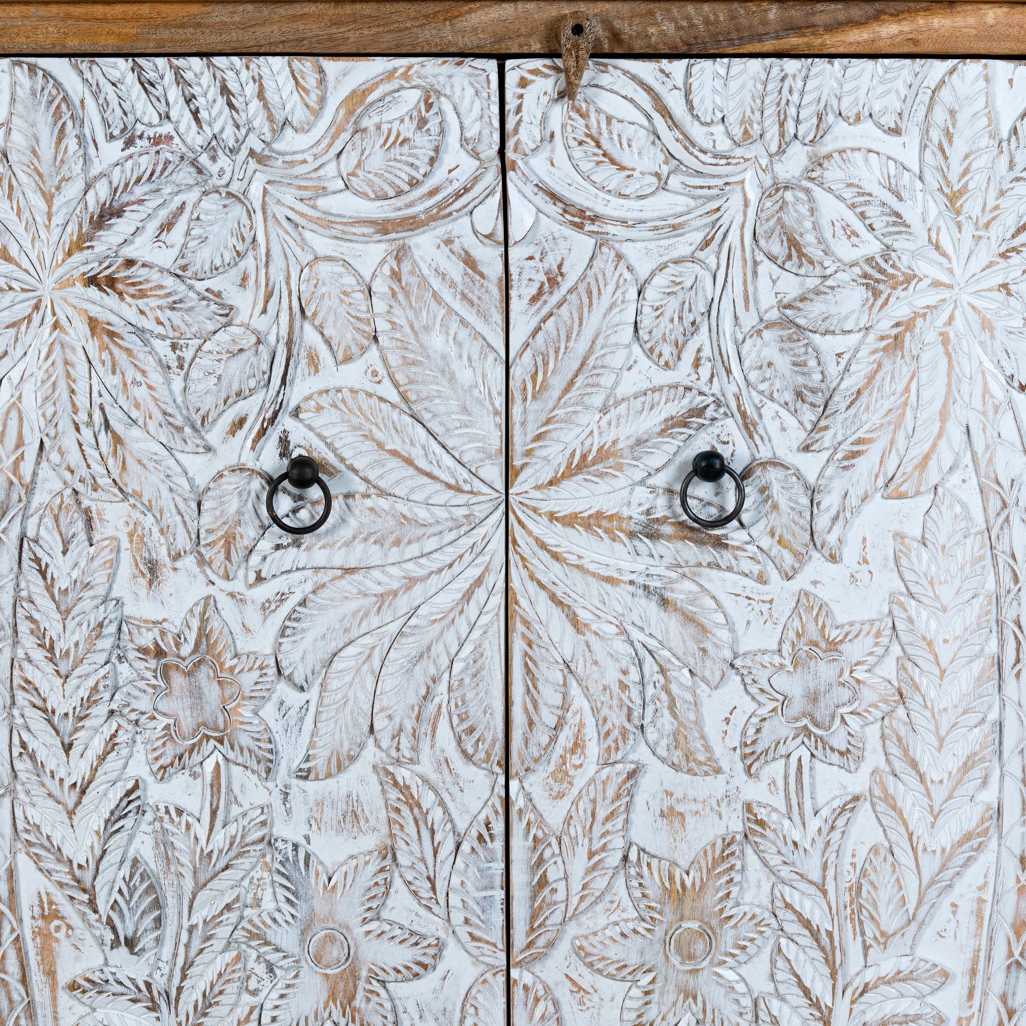 Close up image of a hand-carved mango wood cupboard Utkarsh with whitewashed doors featuring palm tree and botanical motifs. A Mediterranean-inspired piece of Indian furniture combining artisan detail with practical storage.