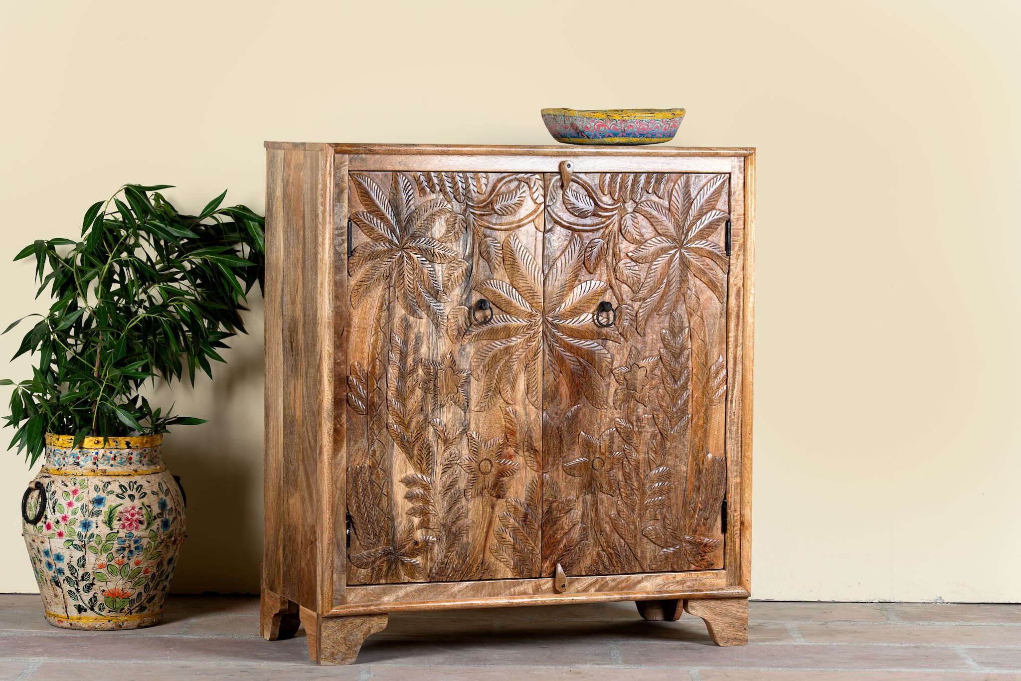 Side angle image of a hand-carved mango wood cupboard Vansh with double doors featuring intricate floral and botanical motifs. A Mediterranean-inspired piece of Indian furniture offering functional storage and timeless artisan detail.