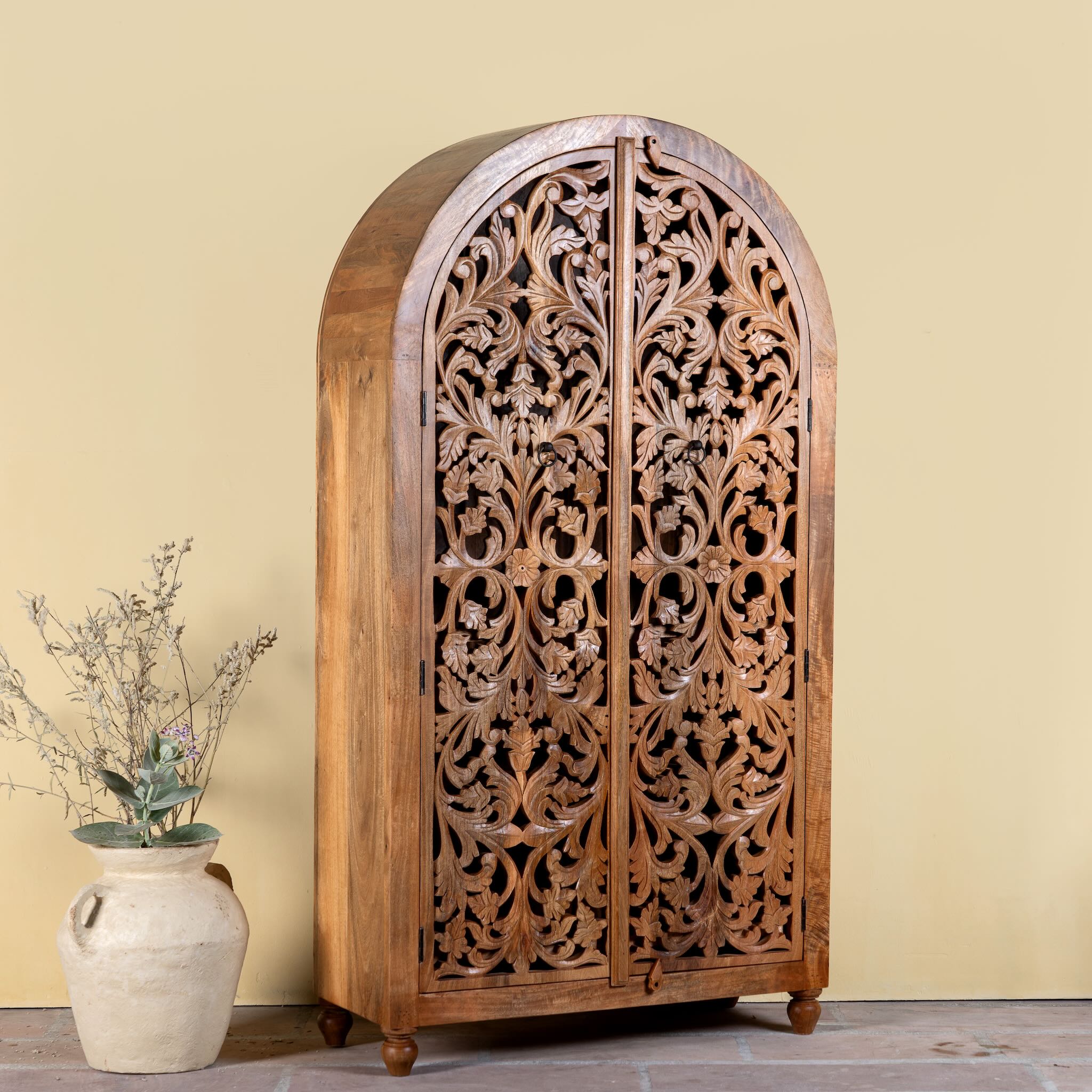 Side angle image of a hand carved wooden wardrobe with arc-shaped cabinet design in solid mango wood – Aranya model by Om Home & Garden