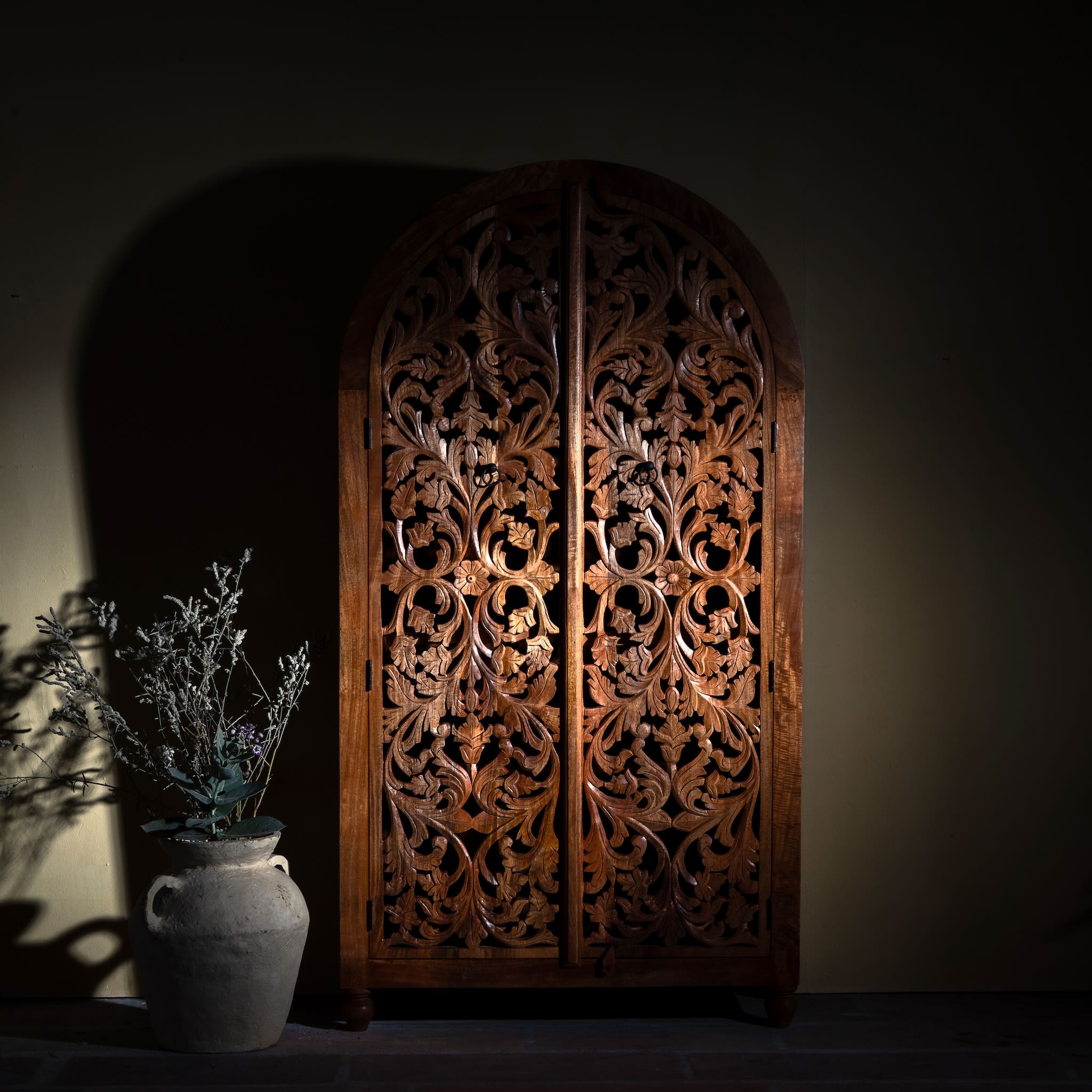 Lifestyle image of a hand carved wooden wardrobe with arc-shaped cabinet design in solid mango wood – Aranya model by Om Home & Garden