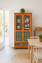 Lifestyle image of a hand-painted teak wood showcase with floral motifs and glass doors – sustainable furniture crafted from recycled wood with traditional Indian artistry.
