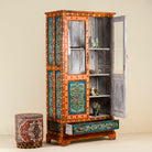Side angle image with open door of a hand-painted teak wood showcase with floral motifs and glass doors – sustainable furniture crafted from recycled wood with traditional Indian artistry.