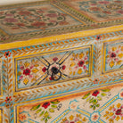 Close up image of a Ziya hand‑painted chest of 8 drawers made from reclaimed wood with floral motifs and iron handles—an artisan piece of painted wooden furniture.