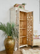 Side angle image with open doors of a hand-carved mango wood cabinet with floral and geometric motifs in white-washed finish – carved wooden furniture with Mediterranean-inspired design.