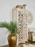 Side angle image of a hand-carved mango wood cabinet with floral and geometric motifs in white-washed finish – carved wooden furniture with Mediterranean-inspired design.